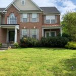 A brick home with overgrown trees and shrubbery